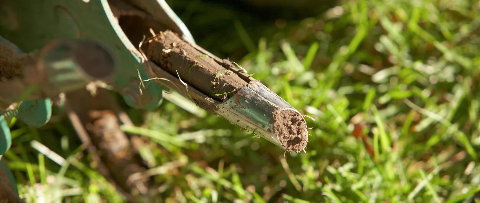 Close-up of a lawn aerator tine ejecting a soil core onto grass, highlighting the core aeration process used to relieve soil compaction and promote healthy turf growth.