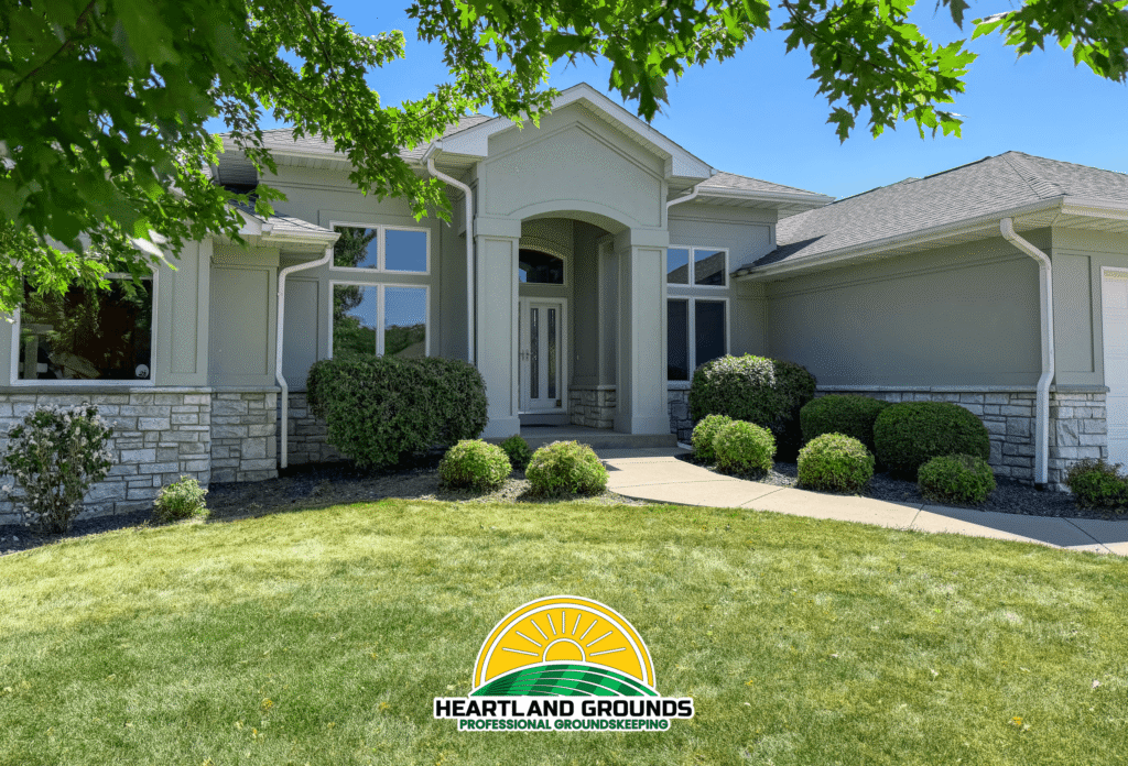 Well-maintained residential landscape featuring freshly trimmed shrubs, clean landscape beds, and a manicured lawn in front of a modern home serviced by Heartland Grounds.